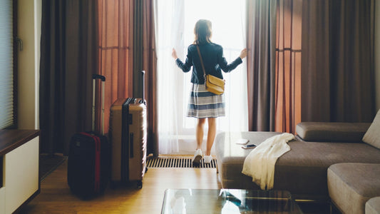 Frau öffnet den Vorhang in einem Hotelzimmer, Koffer stehen daneben